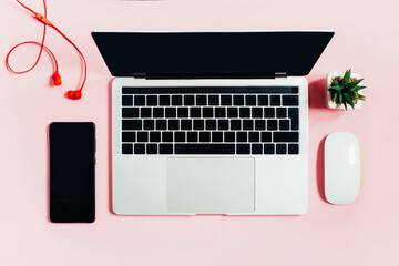 top view of laptop, computer mouse, mobile phone, headphones on pink background