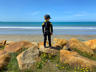 Boy in surfing wetsuit standing on rocks looking at sea