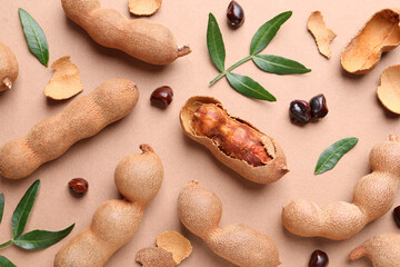 Ripe tamarinds and fresh leaves on beige background, flat lay