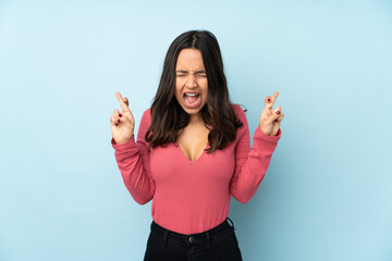 Young mixed race woman isolated on blue background with fingers crossing