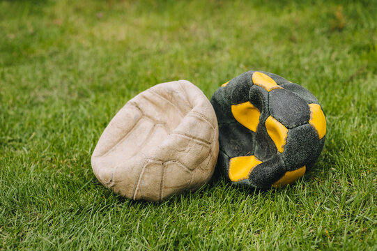 A pair of deflated football old multi-colored balls lie on the green grass of the sports field. Photo of the match. The end of a football player's career.