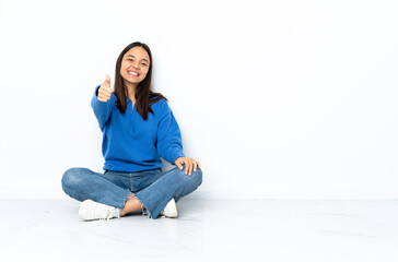 Young mixed race woman sitting on the floor isolated on white background with thumbs up because something good has happened