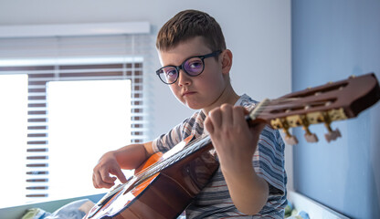 Little boy plays the classical guitar at home, on the bed.