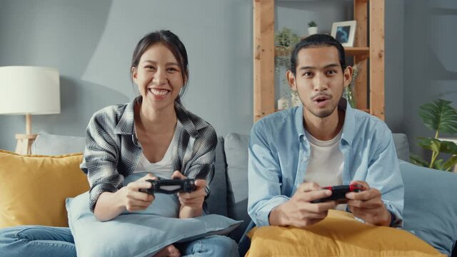 Happy asia young couple man and woman sit on couch use joystick controller play video game spend fun time together in living room. Asian married couple family lifestyle, Couple stay at home concept.