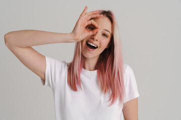 Young woman with pink hair smiling and gesturing ok sign