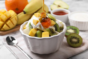 Pouring honey onto delicious fruit salad in bowl on table