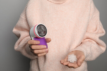 Woman in woolen sweater holding fabric shaver and lint on light grey background, closeup
