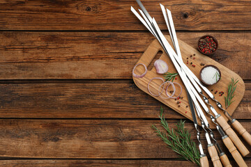 Flat lay composition with metal skewers on wooden table. Space for text