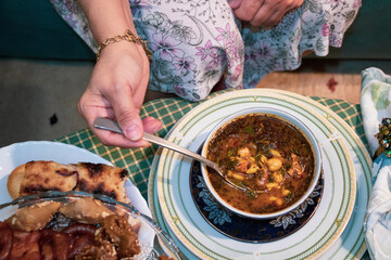 ONE HAND OF AN ADULT WEARS RING AND BRACELET OVER BOWL OF HEALTHY VEGETABLE SOUP, ONE HAND GRASPS A SPOON IN THE BACKGROUND OF OTHER FOOD DISHES, close up