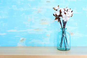 Image of cotton plant flower branch over wooden table and blue background