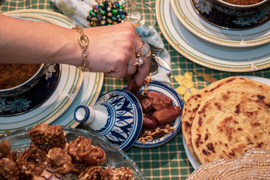ONE HAND OF AN ADULT WEARS RING AND BRACELET OVER BOWL OF HEALTHY VEGETABLE SOUP, ONE HAND GRASPS A DATE IN THE BACKGROUND OF OTHER FOOD DISHES, close up