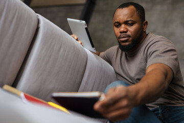 Black unshaven man using tablet computer while working at home