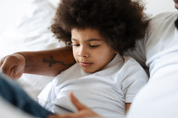 Black father and son using tablet computer while lying in bed