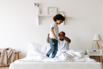 Black boy smiling while playing with her father on bed at home