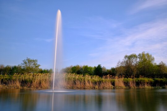 Big water fountain in a lake with a blue sky in the background in Bussy Saint Georges France