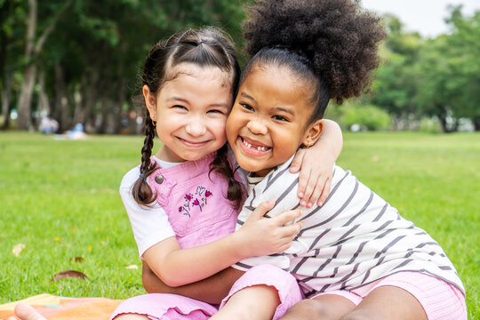 Two African American cheerful little girl sitting on the mat and hugging each other with love in the garden