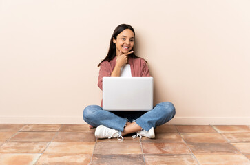 Young mixed race woman with a laptop sitting on the floor happy and smiling