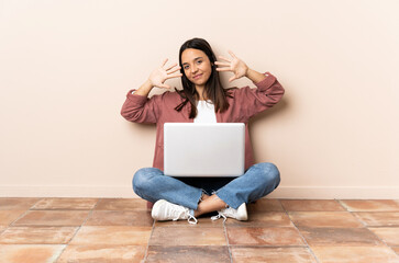 Young mixed race woman with a laptop sitting on the floor counting ten with fingers