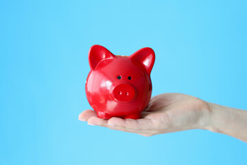 Female hand holding red piggy bank on blue background closeup