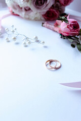 Pink flowers, pearl jewelry and two gold wedding rings on a white background. Wedding concept. Isolated