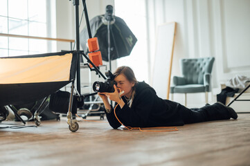 Female photographer lies on the ground in a photo studio and takes pictures on the camera from the bottom of the shooting point.