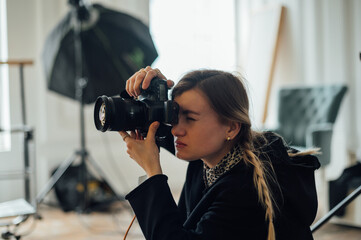 Close-up portrait of a female photographer doing a photo shoot in a photo studio, looking at the camera viewfinder and pressing the shutter button.