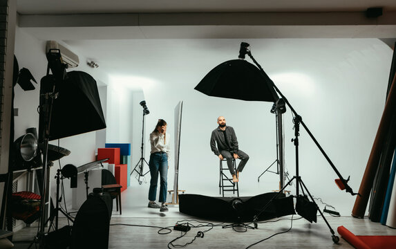 Woman photographer and bearded man model working in a photo studio on a white background with flashes. Backstage photo process photo shoot.