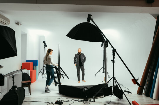 Backstage photo, female photographer and male model working in photo studio on a white background