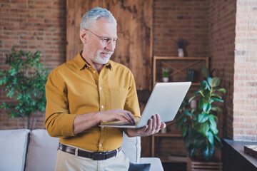 Photo of cheerful aged person look hands hold laptop write email have good mood working from home...