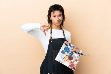 Young artist man holding a palette over isolated background showing thumb down sign