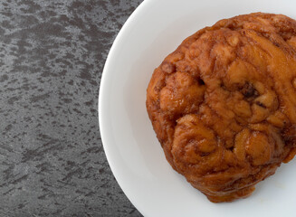 Top close view of an apple fritter on a plate atop a gray tabletop.