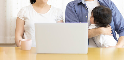 Fototapeta premium 自宅でノートパソコンを使う家族のイメージ（父親、母親、赤ちゃん）