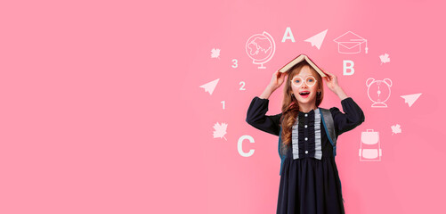 Banner blond girl kid 8-9 y.o. with black glasses and with a book on my head funny looking at camera in isolation on a pink background. Back to school.