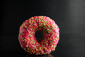 Berliner Donat in pink glaze with colored topping on a black background with a place for text and a copyspace of the delicious food cooking tomorrow's dessert