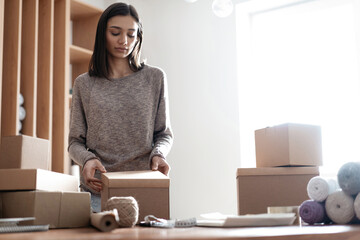 Indian mixed-race female business owner working, packing the order for shipping to customer