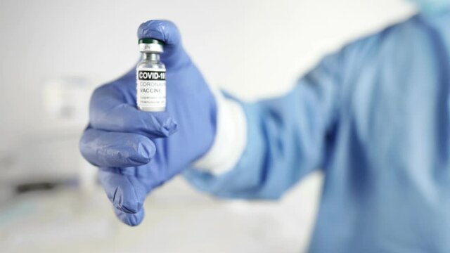 Close up of a doctor or healthcare worker in personal protective kit typing show an ampoules of Covid-19 vaccine in foreground in selective focus. Vaccine Concept of fight against Coronavirus