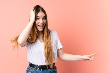 Young caucasian woman isolated on pink background surprised and pointing finger to the side