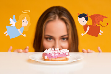 Young woman looking at donut hungrily, wanting to break her diet, feeling doubtful with angel and...