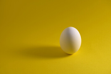 One white egg on a yellow background.