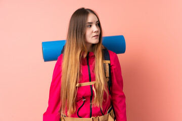 Young mountaineer girl with a big backpack isolated on pink background looking side