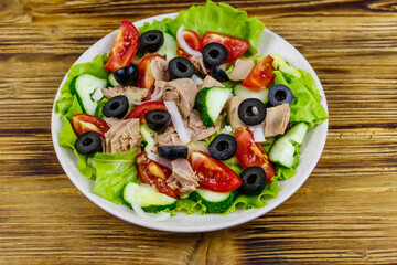 Tasty tuna salad with lettuce, black olives and fresh vegetables on wooden table