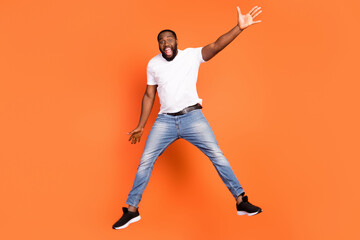 Full length photo of active cheerful afro american man jump up good mood excited isolated on orange color background