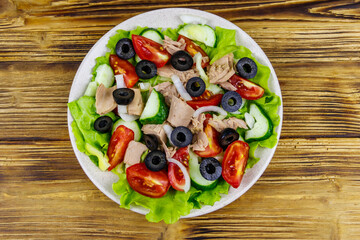 Tasty tuna salad with lettuce, black olives and fresh vegetables on wooden table. Top view