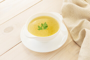 Chicken broth with parsley in a white bowl.