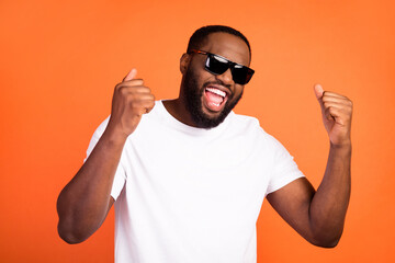 Photo of charming happy young dark skin man winner good mood wear sunglass isolated on orange color background