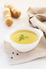 Chicken bone broth with parsley in a white bowl on a towel.