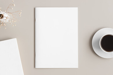 Magazine mockup with a cup of coffee, book and a gypsophila on the beige table.