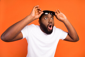Photo of amazed astonished afro american young man look empty space hold glasses isolated on orange color background - obrazy, fototapety, plakaty