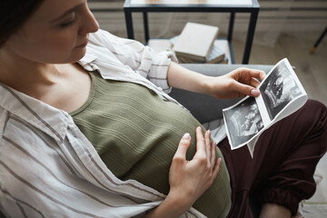 Pregnant woman sitting on sofa and resting she looking at x-ray image and waiting for the birth of her baby