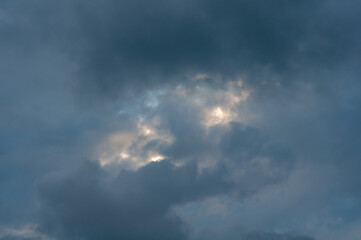 Covered with dark blue clouds with small gap through which sun's rays and bright blue sky break through.